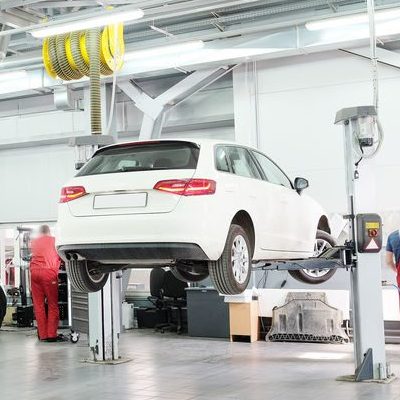 An auto car lift raised a few feet off the ground with a white van on it.