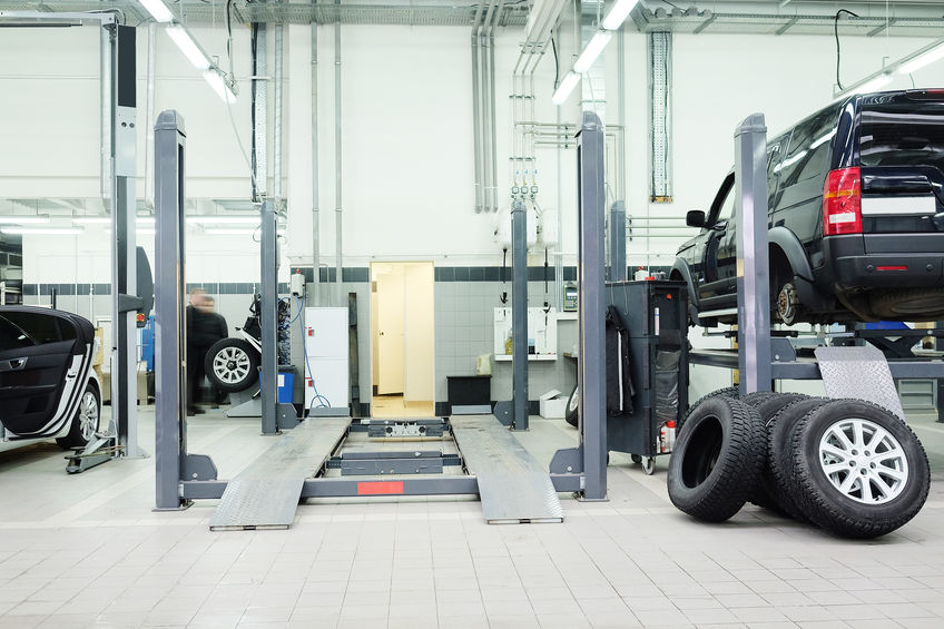 An empty auto car lift in the center of a mechanic shop with a cut off one on the right with a black van on it.