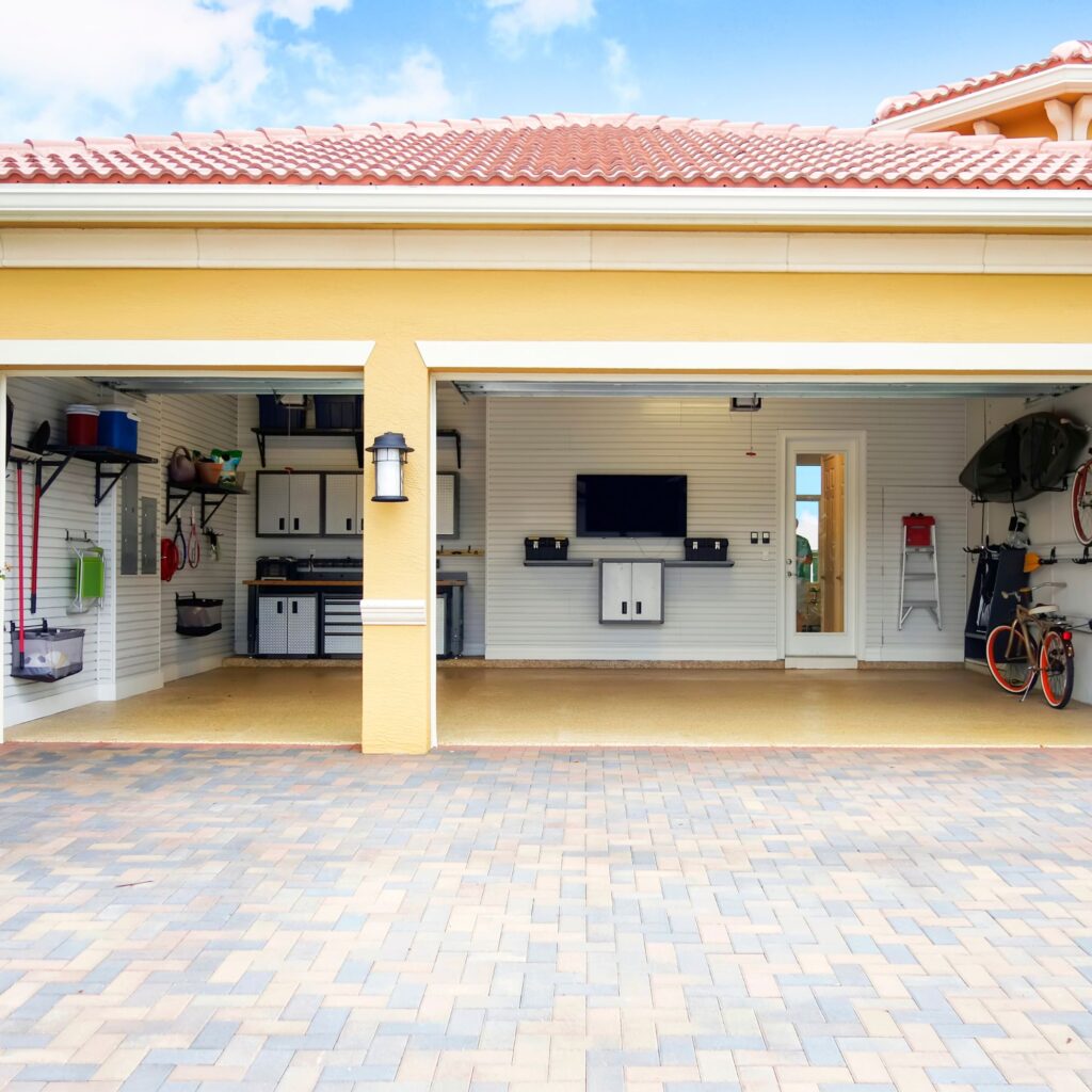neatly organized garage with television, paver driveway, and tile roofing